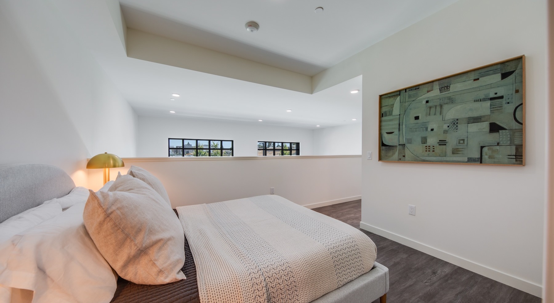 a room with a bed and a picture on the wall next to a railing looking down