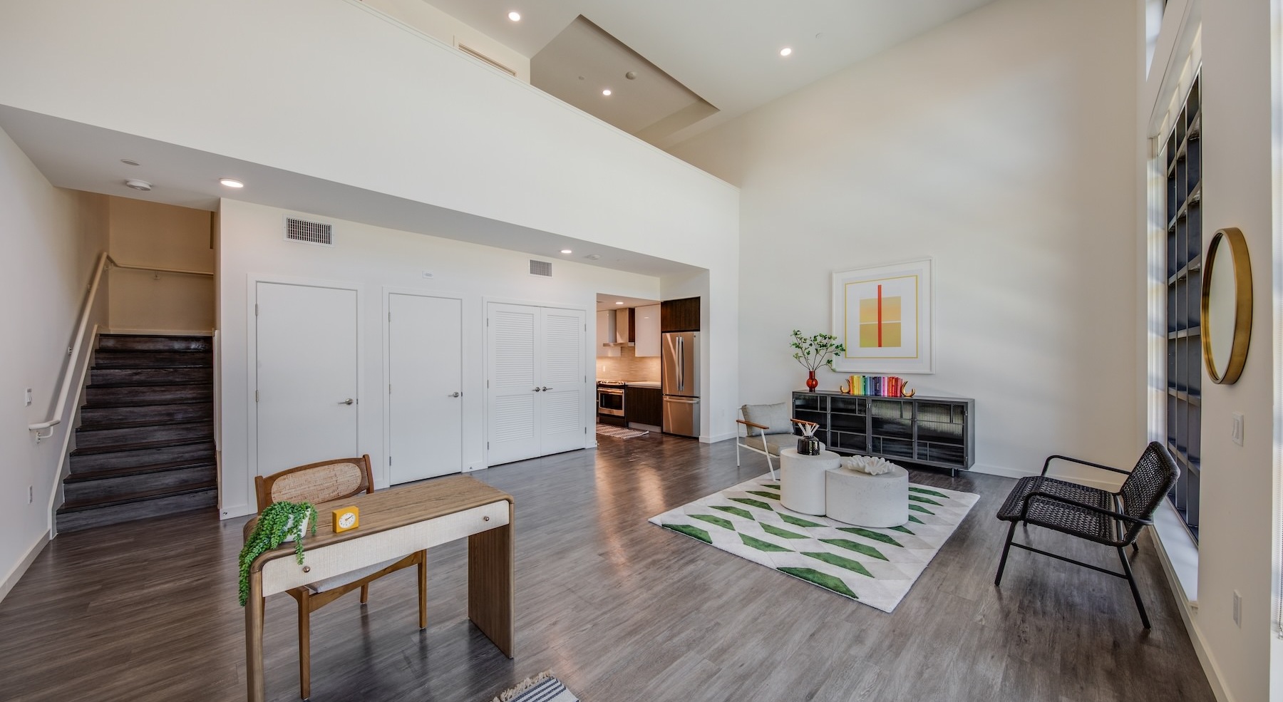 a room with large windows, chairs and a desk with a chair and a staircase